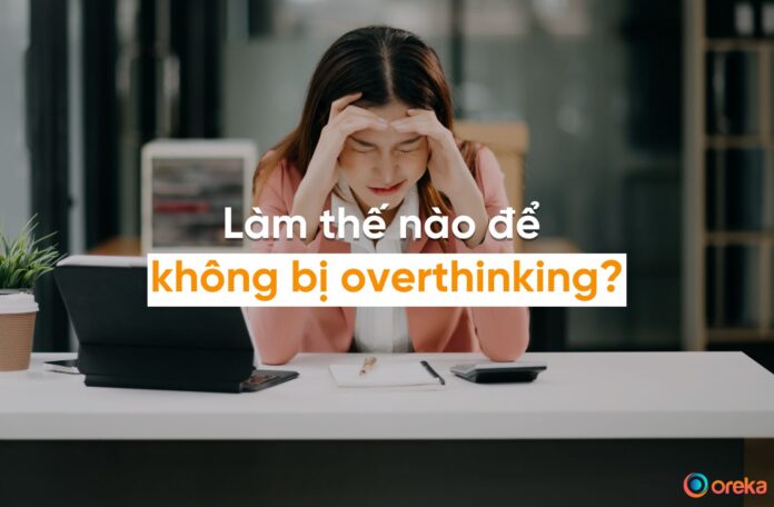 overthinking là gì, hình ảnh cô gái trẻ đang ôm đầu suy nghĩ trước bàn làm việc