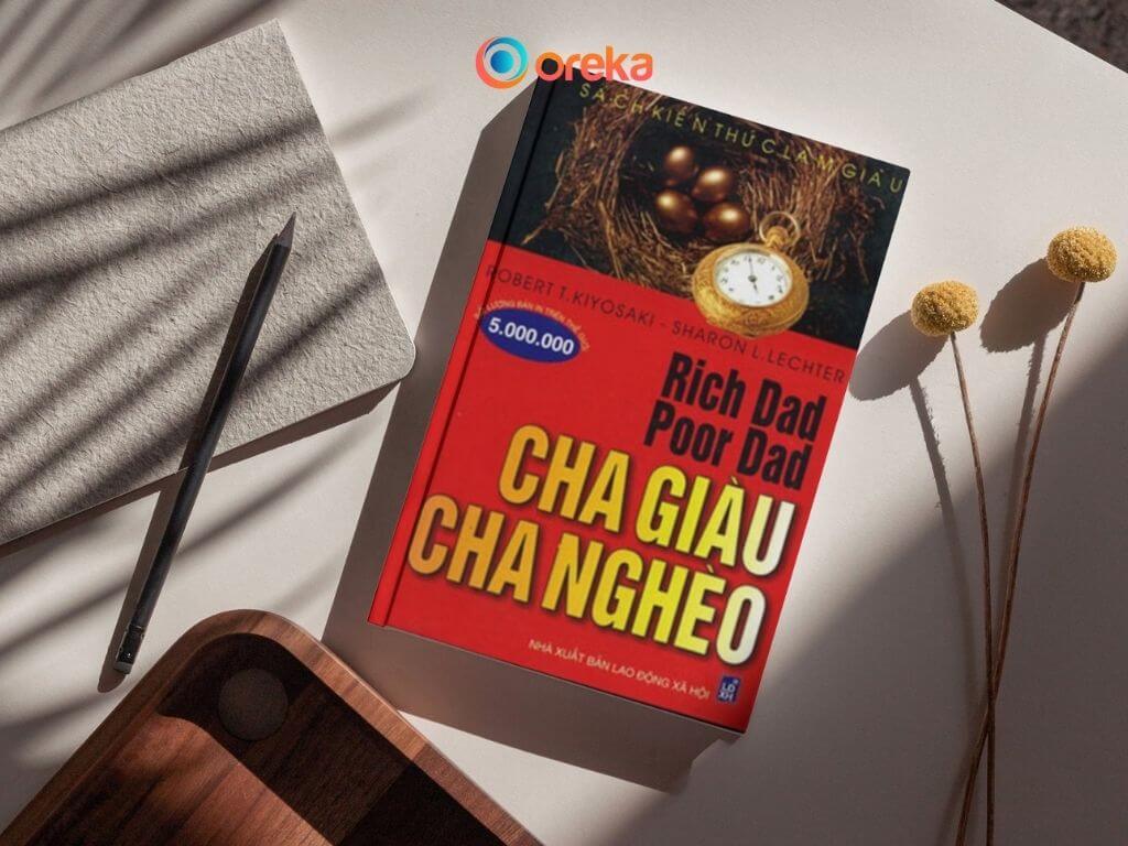 Cha Giàu Cha Nghèo: Review Sách Hay Làm Giàu 3 Review Cha giàu cha nghèo, hình ảnh cuốn sách được đặt trên bàn, bên cạnh có 1 cái bút, 1 cuốn sổ, 1 khay gỗ và 2 bông hoa khô