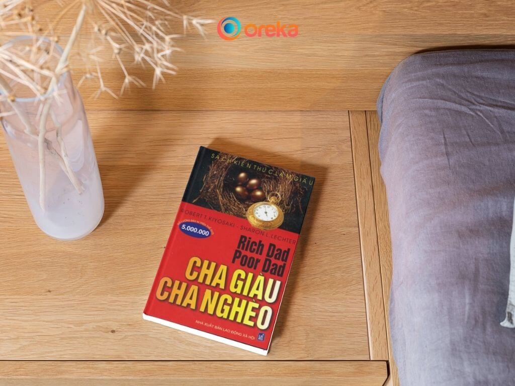 Cha Giàu Cha Nghèo: Review Sách Hay Làm Giàu 2 Cha giàu cha nghèo review, hình ảnh cuốn sách được ở tủ gỗ đầu giường bên cạnh có một bình hoa khô