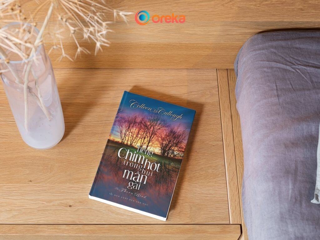 tiếng chim hót trong bụi mận gai review, hình ảnh cuốn sách được đặt ở tủ đầu giường, bên cạnh có 1 bình hoa khô