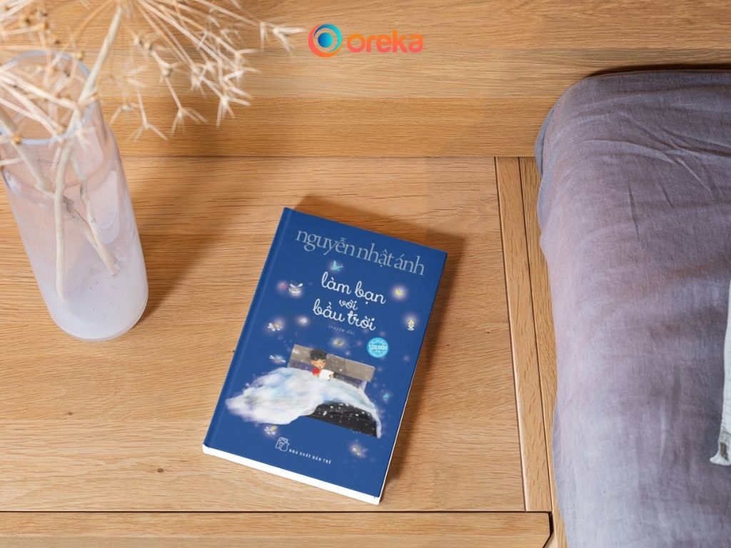 Sách làm bạn với bầu trời. Hình ảnh cuốn sách được đặt ở tủ gỗ đầu giường, bên cạnh có một bình hoa khô.