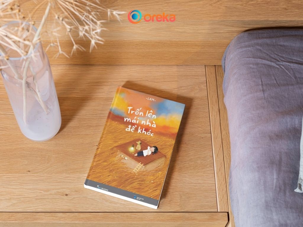 sách Trốn lên mái nhà để khóc review. Hình ảnh cuốn sách được đặt cạnh tủ gỗ đầu giường, bên cạnh có một bình hoa khô.