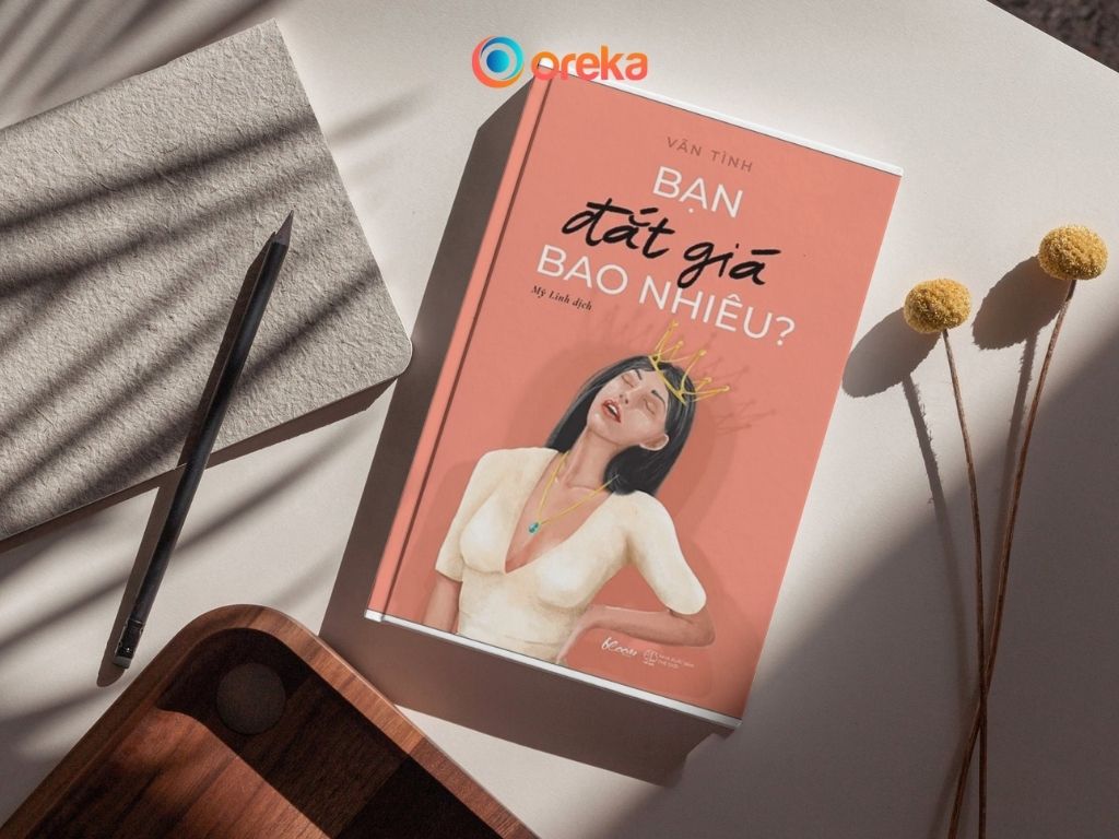 sách Bạn đắt giá bao nhiêu. Hình ảnh cuốn sách được đặt trên bàn, bên cạnh có một cành hoa khô, 1 cuốn sổ, 1 cây bút và một 1/4 của khay gỗ.